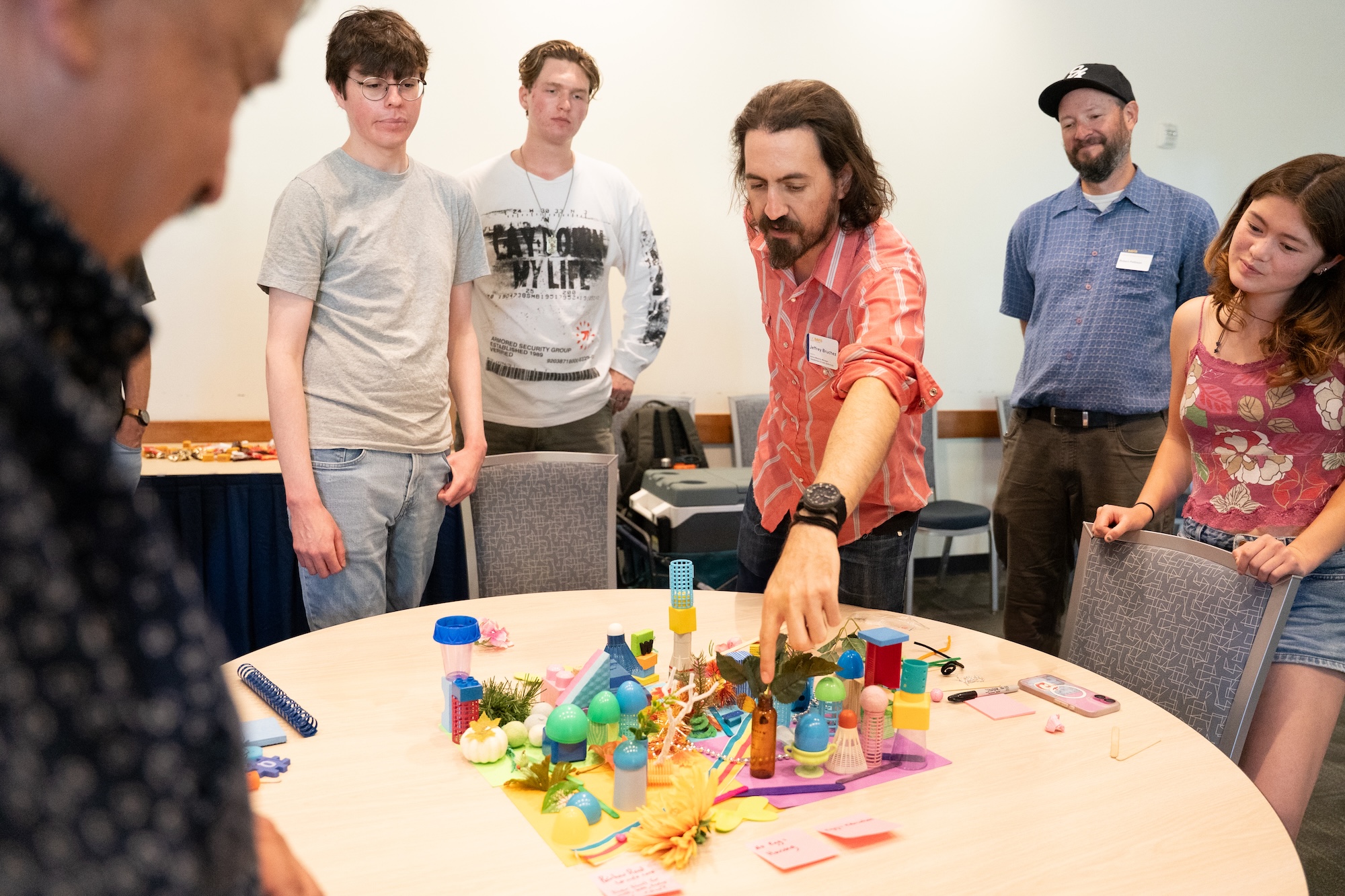Jeff Bruchez, Robert Pattison and a group of people stand around a table with a diorama as Jeff points to a part of the structure.