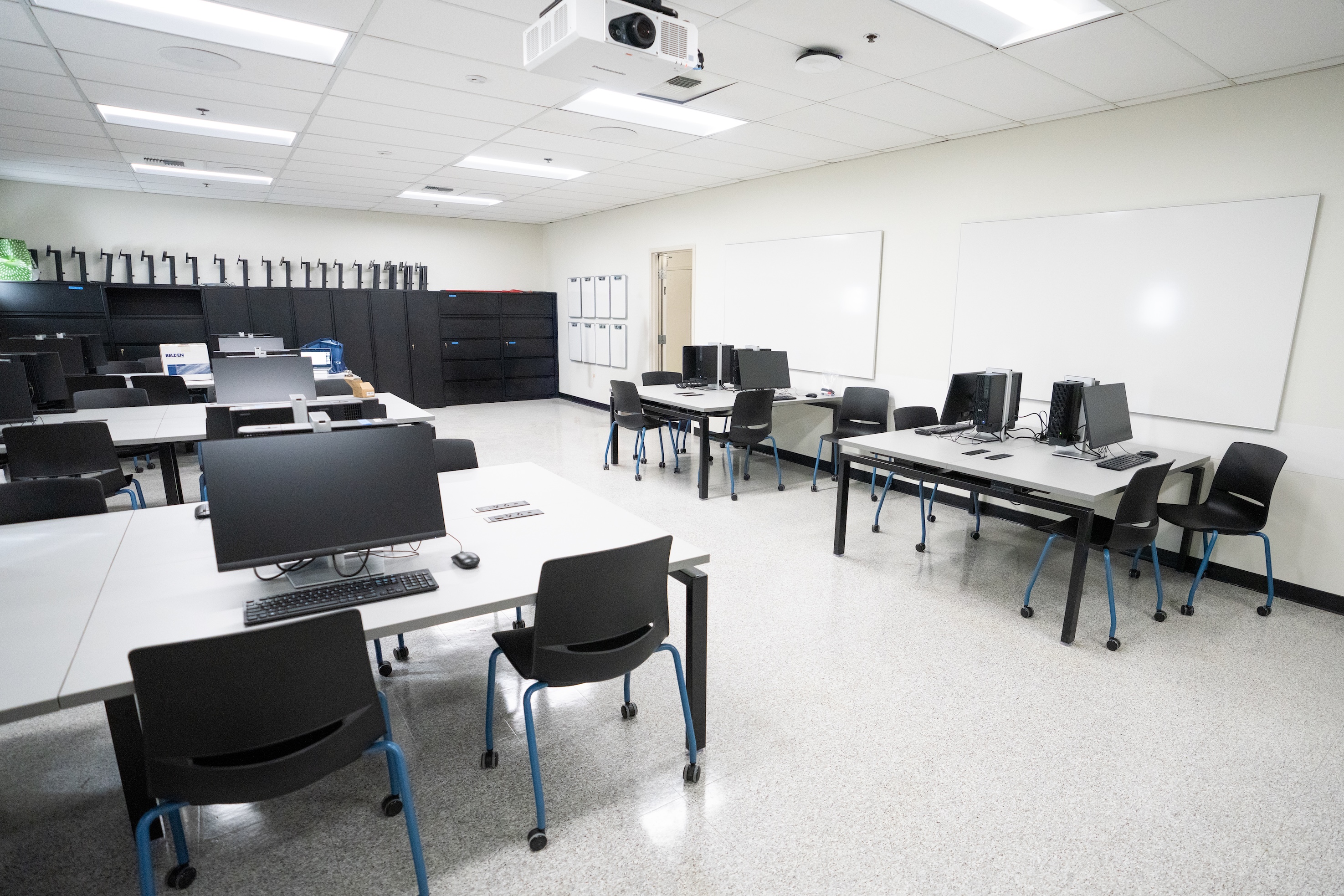 Empty computer lab with rows of desktop monitors, chairs, and whiteboards.