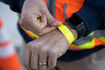 Construction Worker at the Teaching and Learning Complex puts on a wristband after getting their symptom survey.