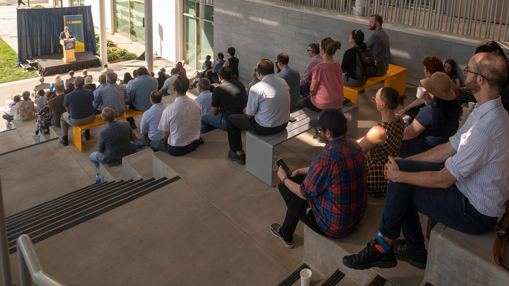 A crowd seated on the stairs on the south side on the Teaching and Learning Center, listening to an address by Chancellor Gary May