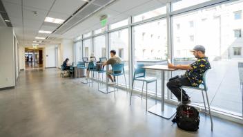 People working on laptops at tables near large windows in the Chemistry Building addition