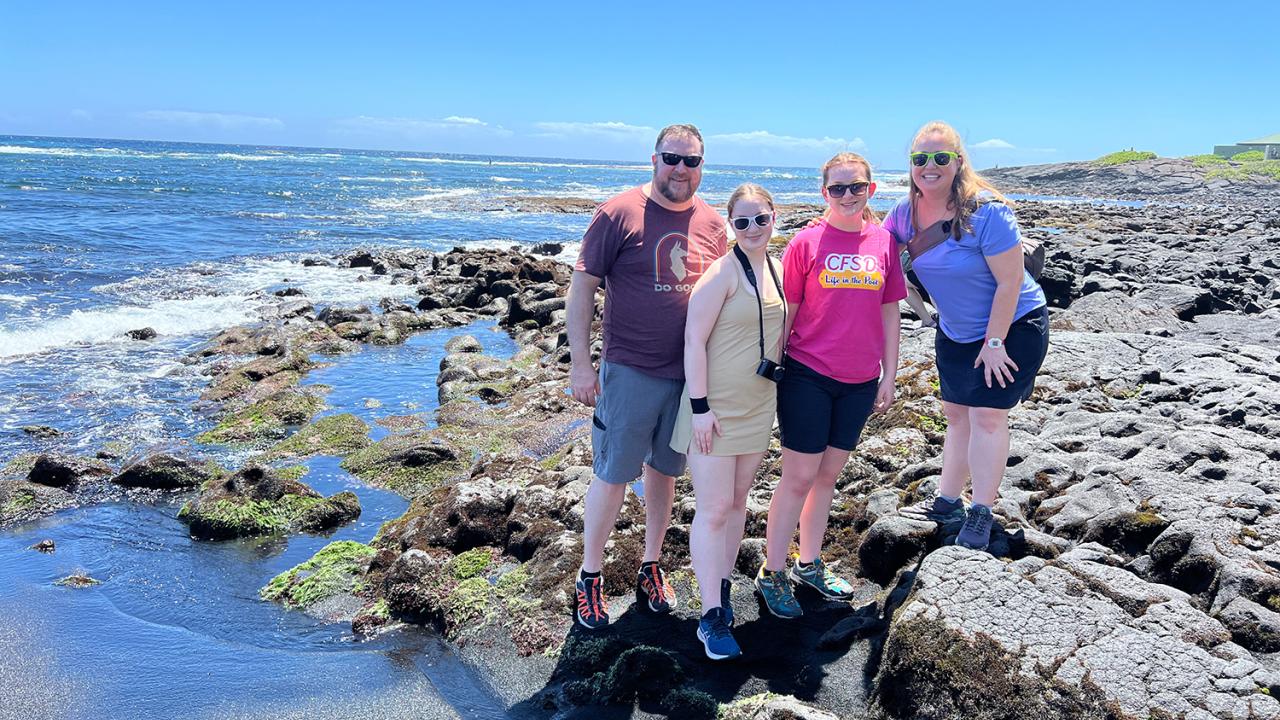 Eric O'Brien posing with family at a rocky beach shore.