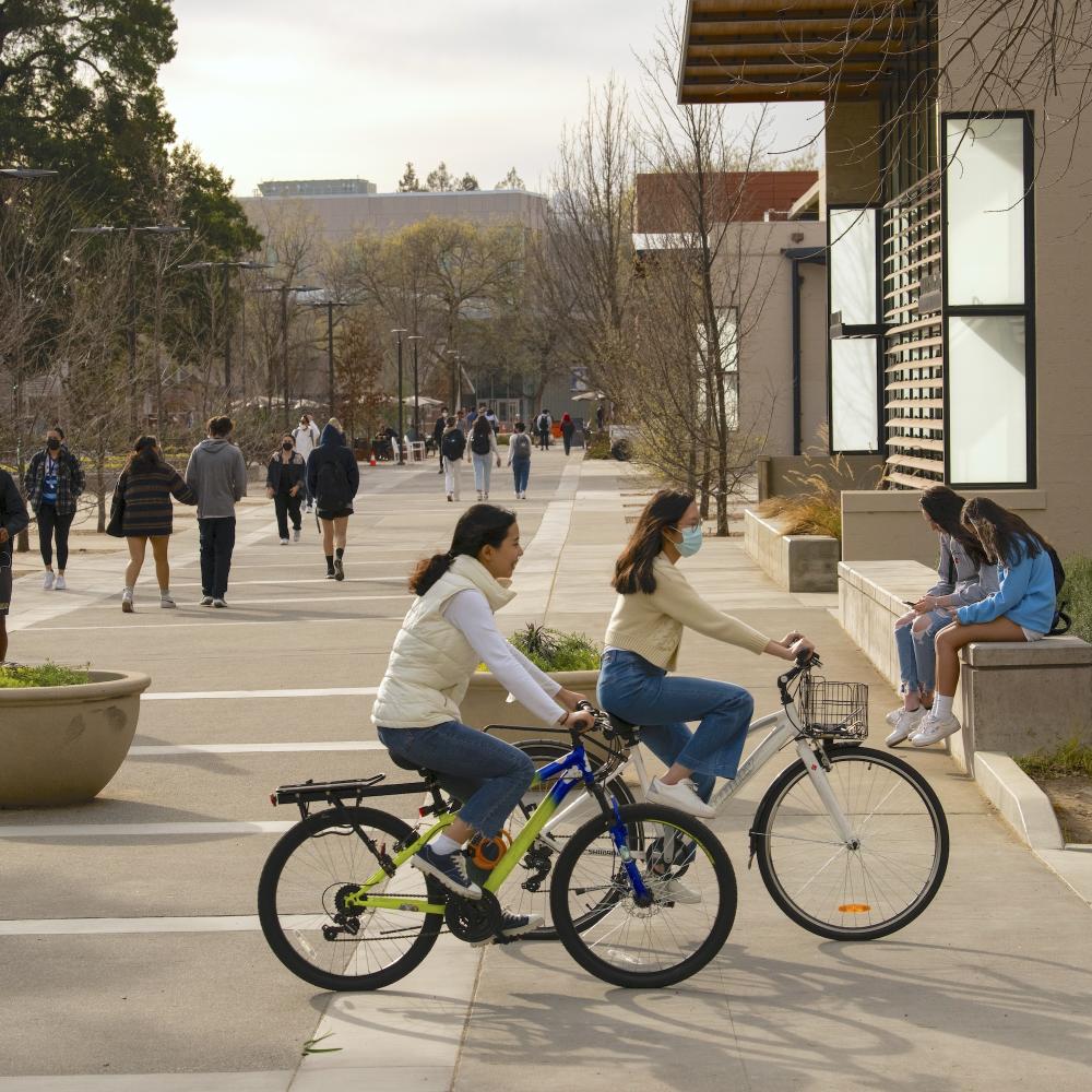 Students ride their bikes between Walker Hall and Shields Library
