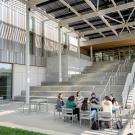 Group of people sit at a table near the large staircase outside the Teaching and Learning Complex