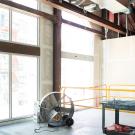 Interior under construction with exposed ceiling beams, large windows, scaffold and tools.